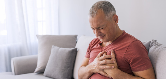 Severe heartache, man suffering from chest pain, having heart attack or painful cramps, pressing on chest with painful expression. Photo of Mature man suffering from chest pain at home during the day.
