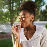 happy african american woman smoking marijuana joint in back yard