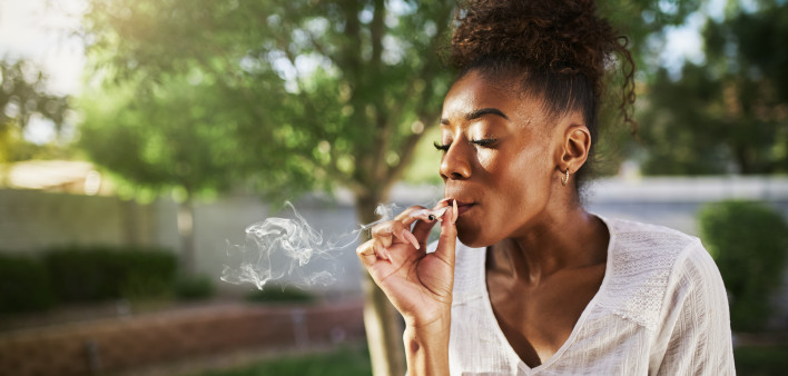happy african american woman smoking marijuana joint in back yard