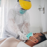 Doctor applying face mask to a senior man who is lying in hospital bed because of coronavirus infection