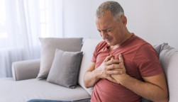 Severe heartache, man suffering from chest pain, having heart attack or painful cramps, pressing on chest with painful expression. Photo of Mature man suffering from chest pain at home during the day.