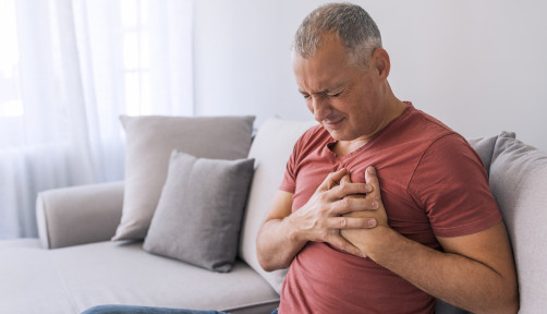 Severe heartache, man suffering from chest pain, having heart attack or painful cramps, pressing on chest with painful expression. Photo of Mature man suffering from chest pain at home during the day.