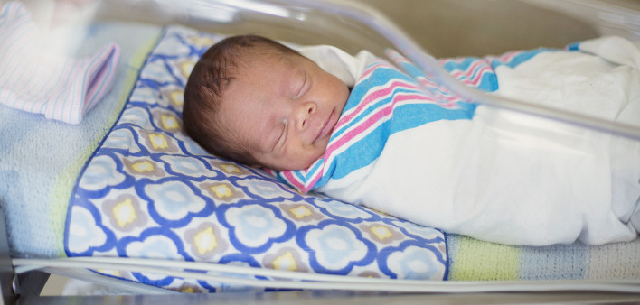 Sleeping baby boy resting in a hospital crib in a hospital delivery room.