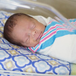Sleeping baby boy resting in a hospital crib in a hospital delivery room.