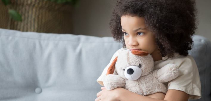 Upset lonely african kid girl holding teddy bear looking away