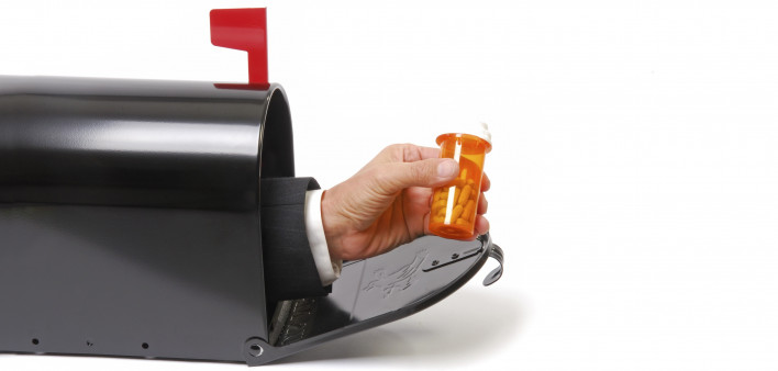 a hand holding a prescription coming out of a mailbox