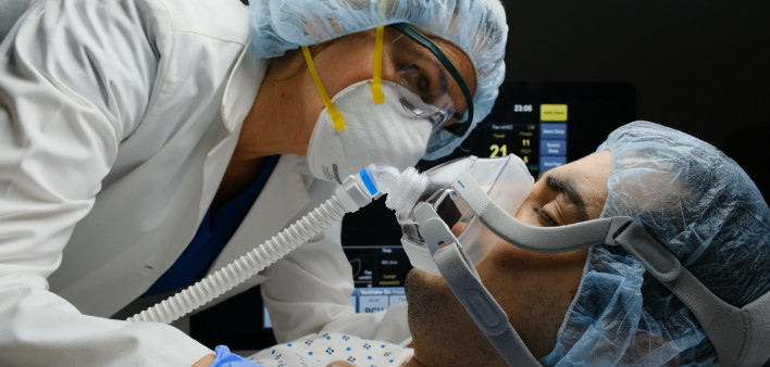Female caucasian doctor checking on Covid-19 infected patient while connected to a ventilator at a hospital room