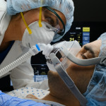 Female caucasian doctor checking on Covid-19 infected patient while connected to a ventilator at a hospital room