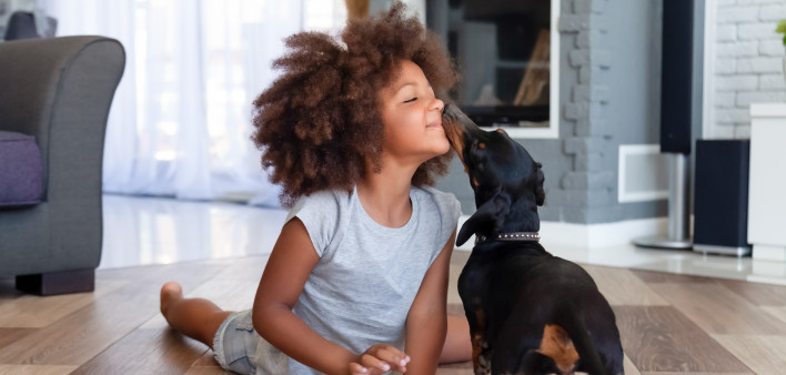 Funny little African American girl lying on floor coloring picture having fun with dog,