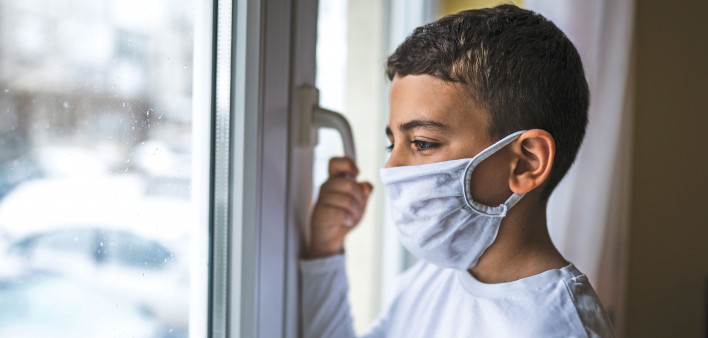 small boy wearing mask looking out window