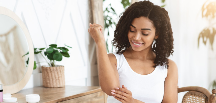 Dry Elbows Treatment. Smiling Black Woman Applying Moisturising Cream