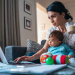 Young modern mother with a baby using laptop at home