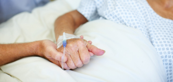 Closeup shot of an elderly man holding his wife's hand while she is ill in the hospital