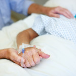 Closeup shot of an elderly man holding his wife's hand while she is ill in the hospital